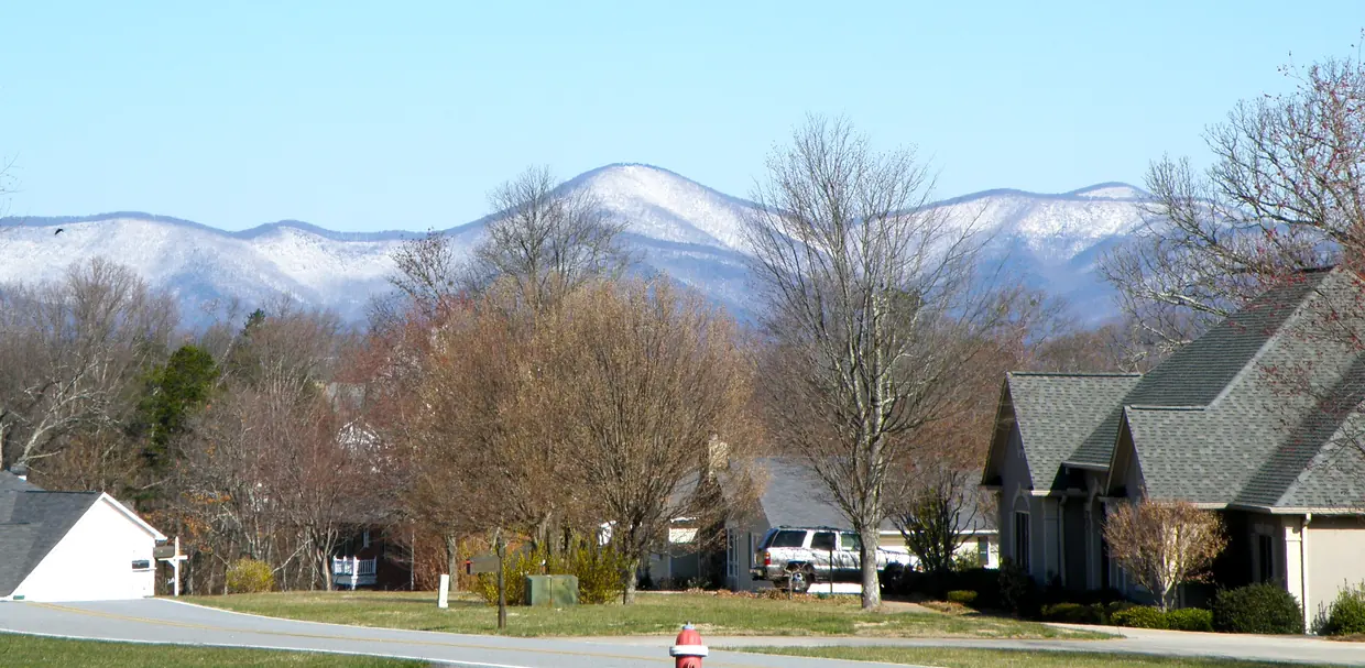 A quiet residential street in late winter, lawns and bare trees, with a long ridge of snow-dusted mountains under a pale blue sky behind.